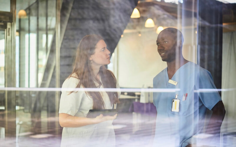 Två läkare som samtalar, fotograferade bakom en glasvägg